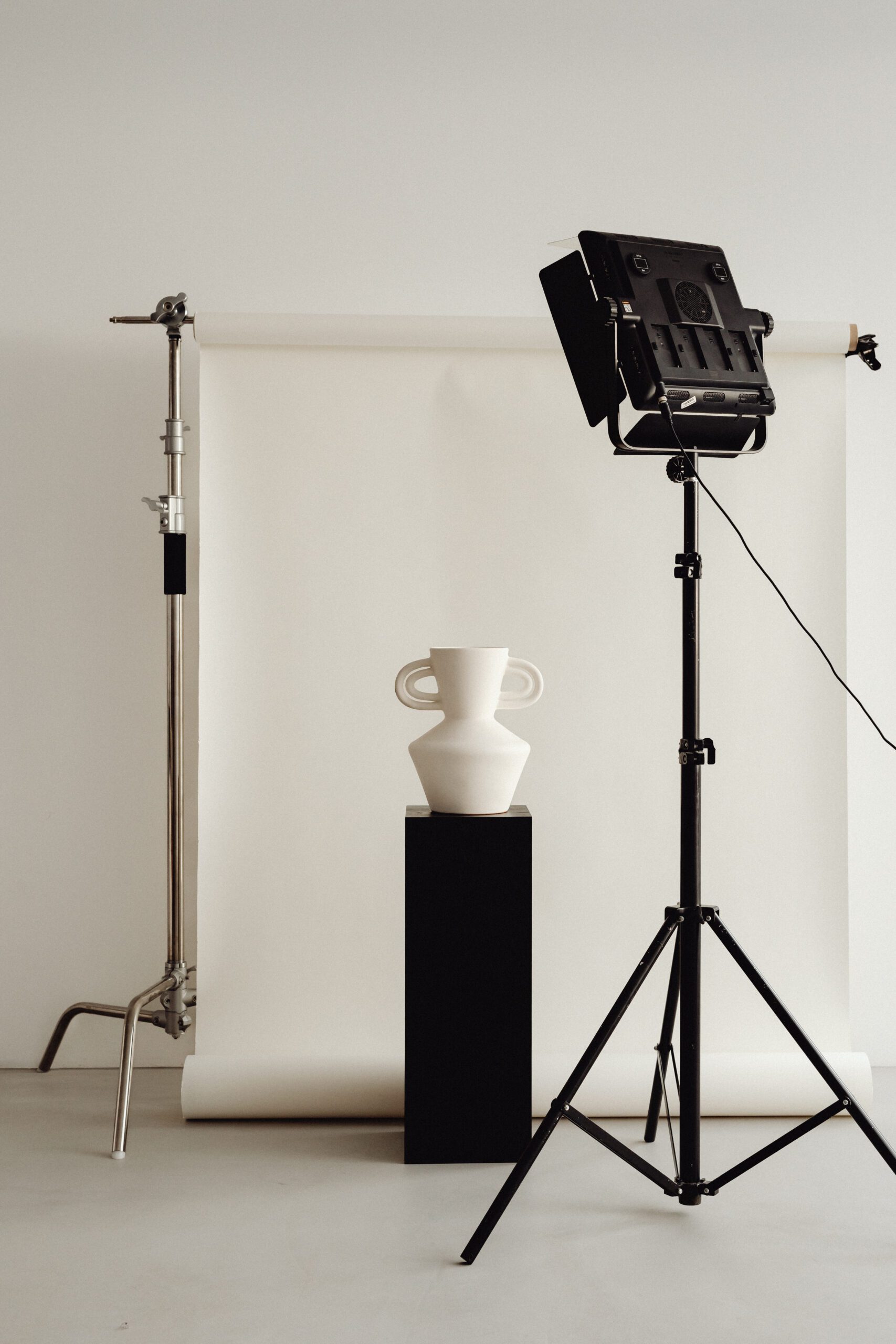 kaboompics_photo-studio-interior-c-stand-lighting-tripod-photo-backdrop-led-lamp-29840 (1) A person with short brown hair is partially obscured by a sheer curtain. They are wearing a white collared shirt and a delicate chain necklace. A dangling earring with a small, translucent pendant is visible. The background is softly blurred, creating a serene atmosphere.